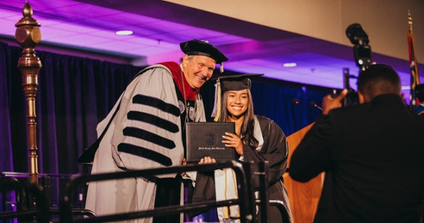 MGA President Chris Blake poses with a graduate for a photo as she crosses the stage at commencement.