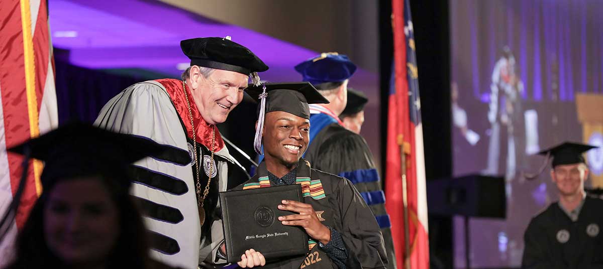 President Blake handing a degree to an MGA graduate as he crosses the stage.